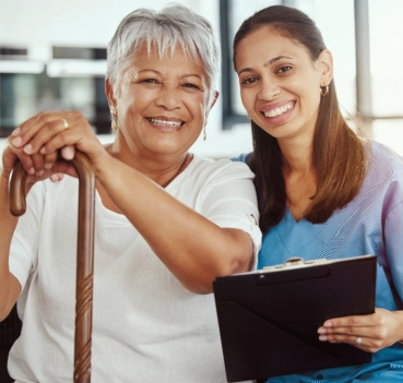 Caregiver smiling with elderly woman holding cane