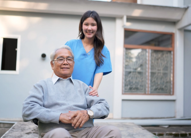 Caregiver standing behind senior man in wheelchair outdoors