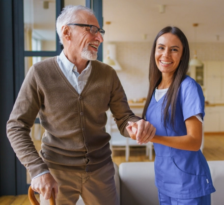 Caregiver holding hands with senior man walking indoors