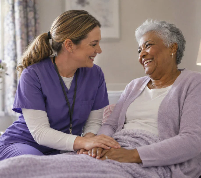 Smiling caregiver in purple scrubs holding the hands of a laughing elderly woman