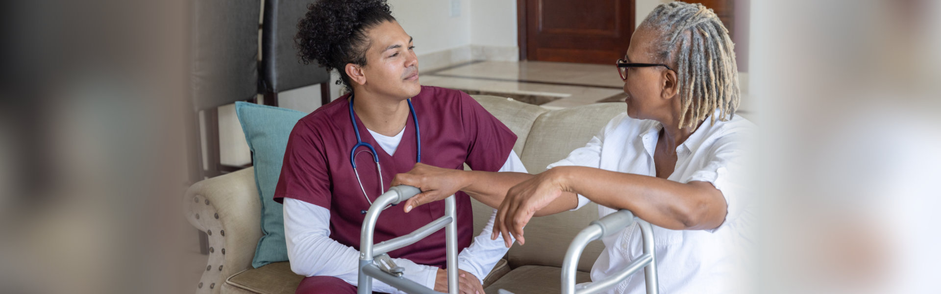 Caregiver in maroon scrubs talking with an older woman who is using a walker